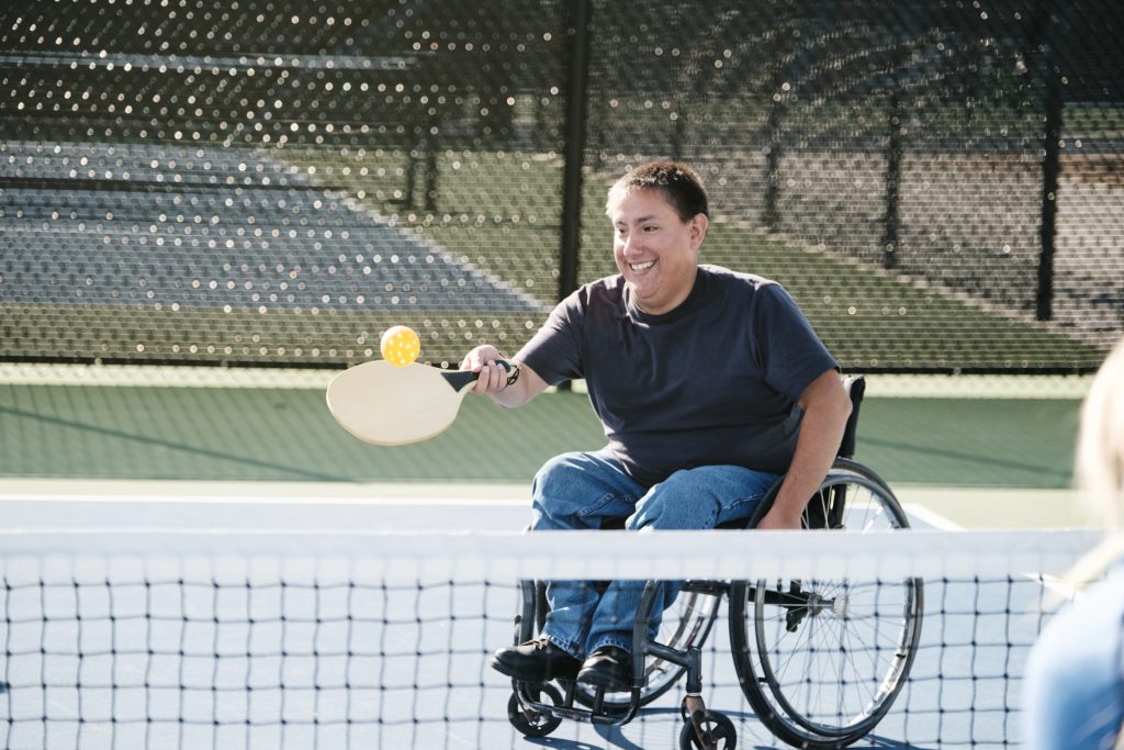 A young man in a wheelchair playing the game of pickleball on a court.